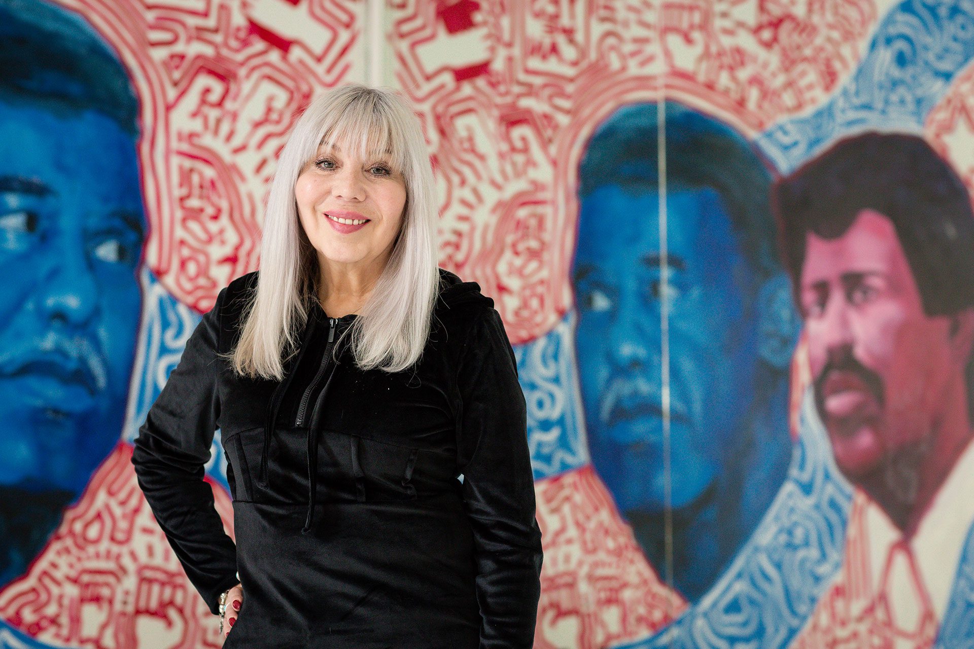 Organizer and pastor Emma Lozano, wearing a black hoodie, poses in front of a mural that depicts Chicago mayor Harold Washington and Lozano’s brother, Rudy Lozano.