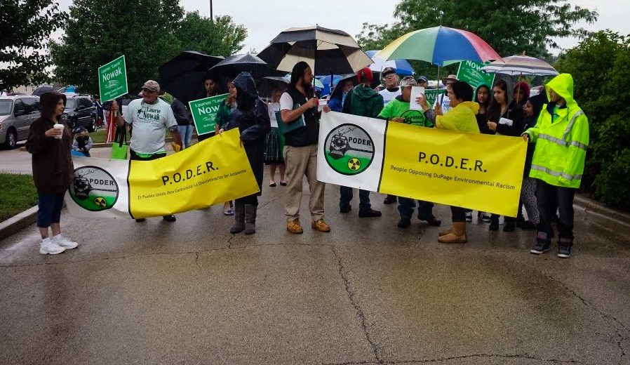 Members of Immigrant Solidarity DuPage march in the street with banners that say P.O.D.E.R on a rainy day