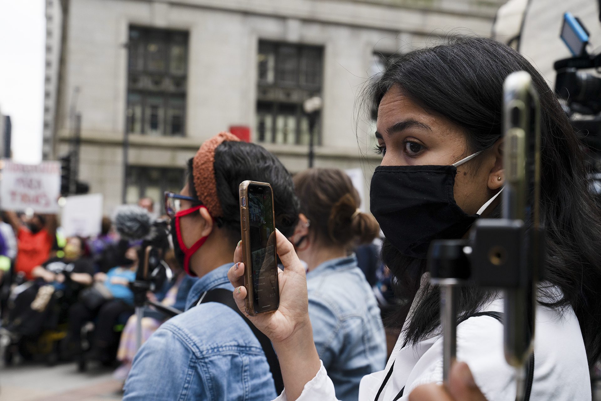 une journaliste enregistrant un rassemblement avec son téléphone et portant un masque