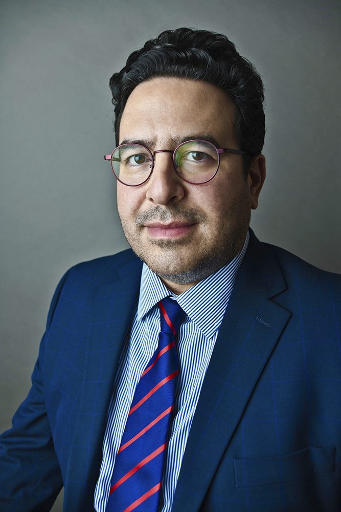 headshot of author Mike Amezcua wearing a suit and tie and purple glasses