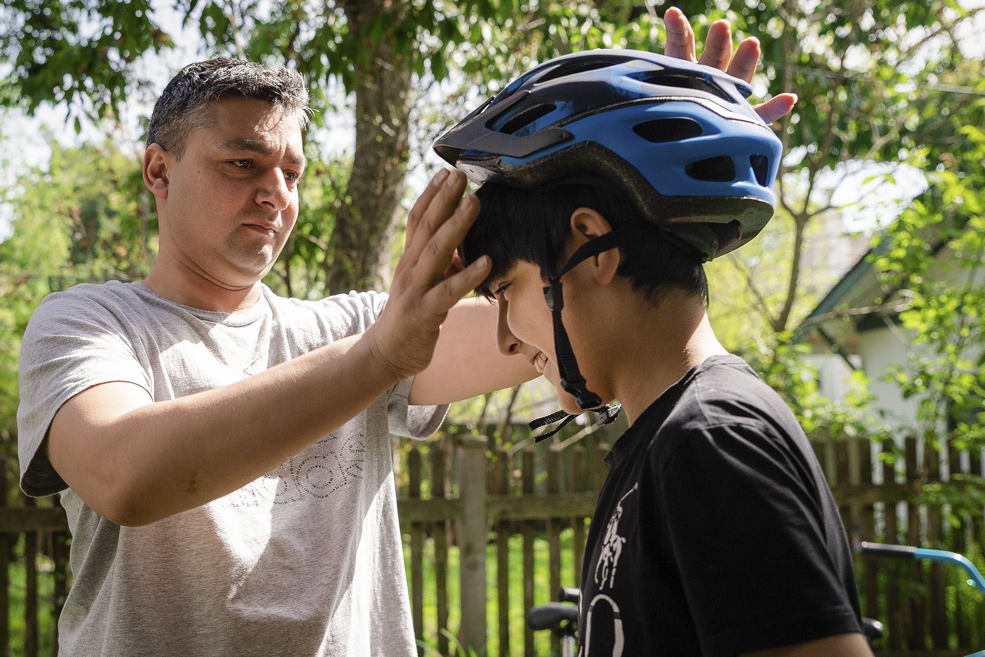Mohammad Aimal puts a bike helmet on his nephew, Yahya Nazari