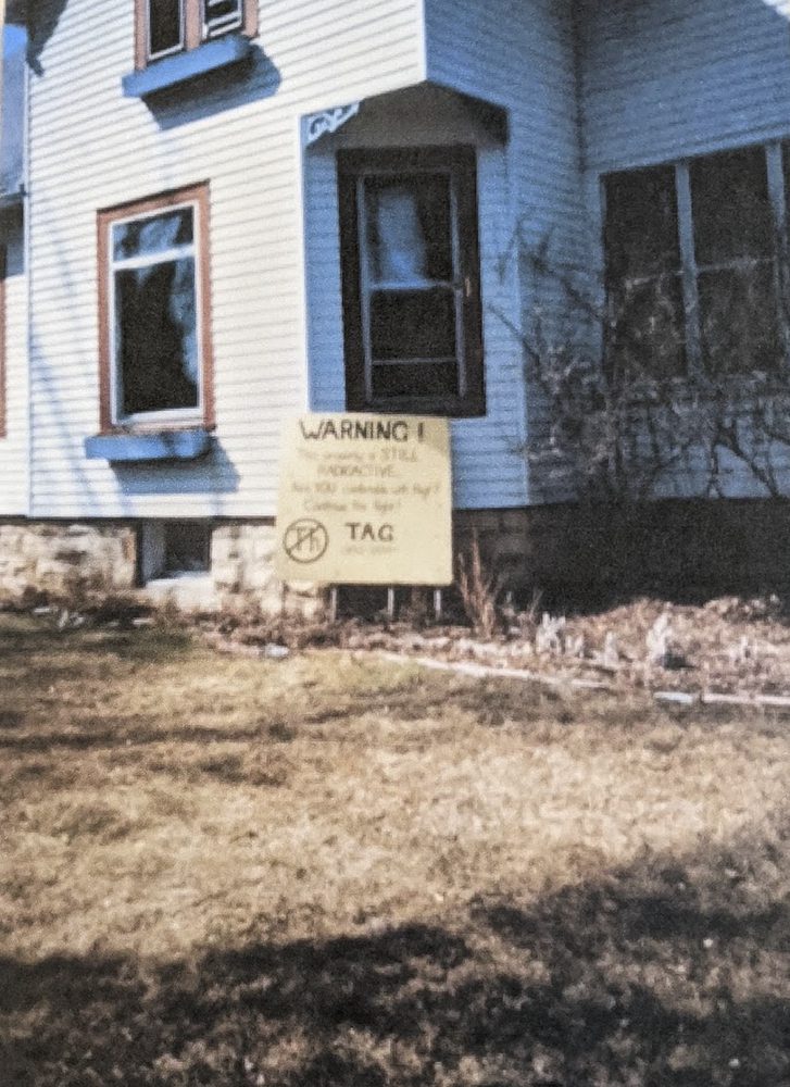 Un cartel escrito a mano fuera de una casa dice &quot;¡Advertencia! Esta propiedad sigue siendo radiactiva&quot; en West Chicago, Illinois, en la década de 1990. La &quot;Th&quot; rodeada y tachada significa torio, un metal radiactivo.