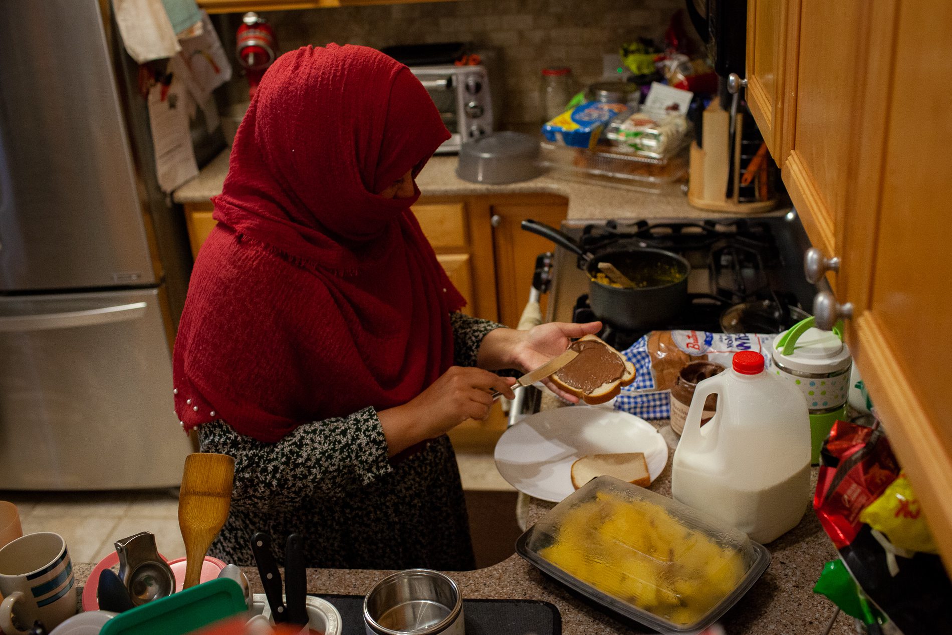 Huma Quadri wearing a red hijab spreads Nutella on a white piece of bread