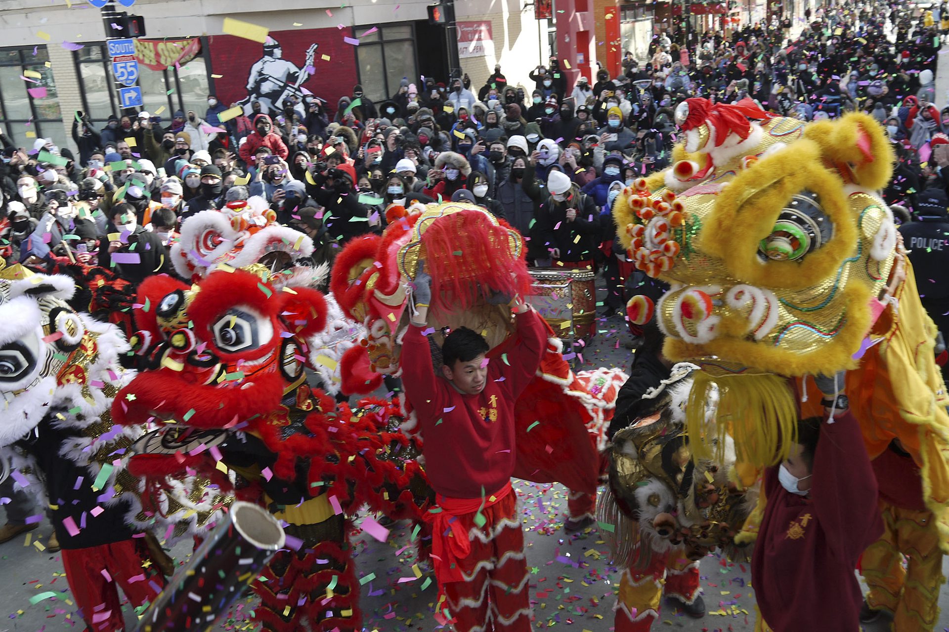 hundreds fill the streets with confetti in the air and a several people with dragon costumes in the foreground