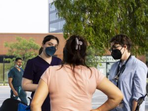 Medical students and doctors wearing masks talk to a woman outside a police station.