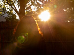 Ada views the sunset in her suburban backyard as sun rays illuminate her long hair.