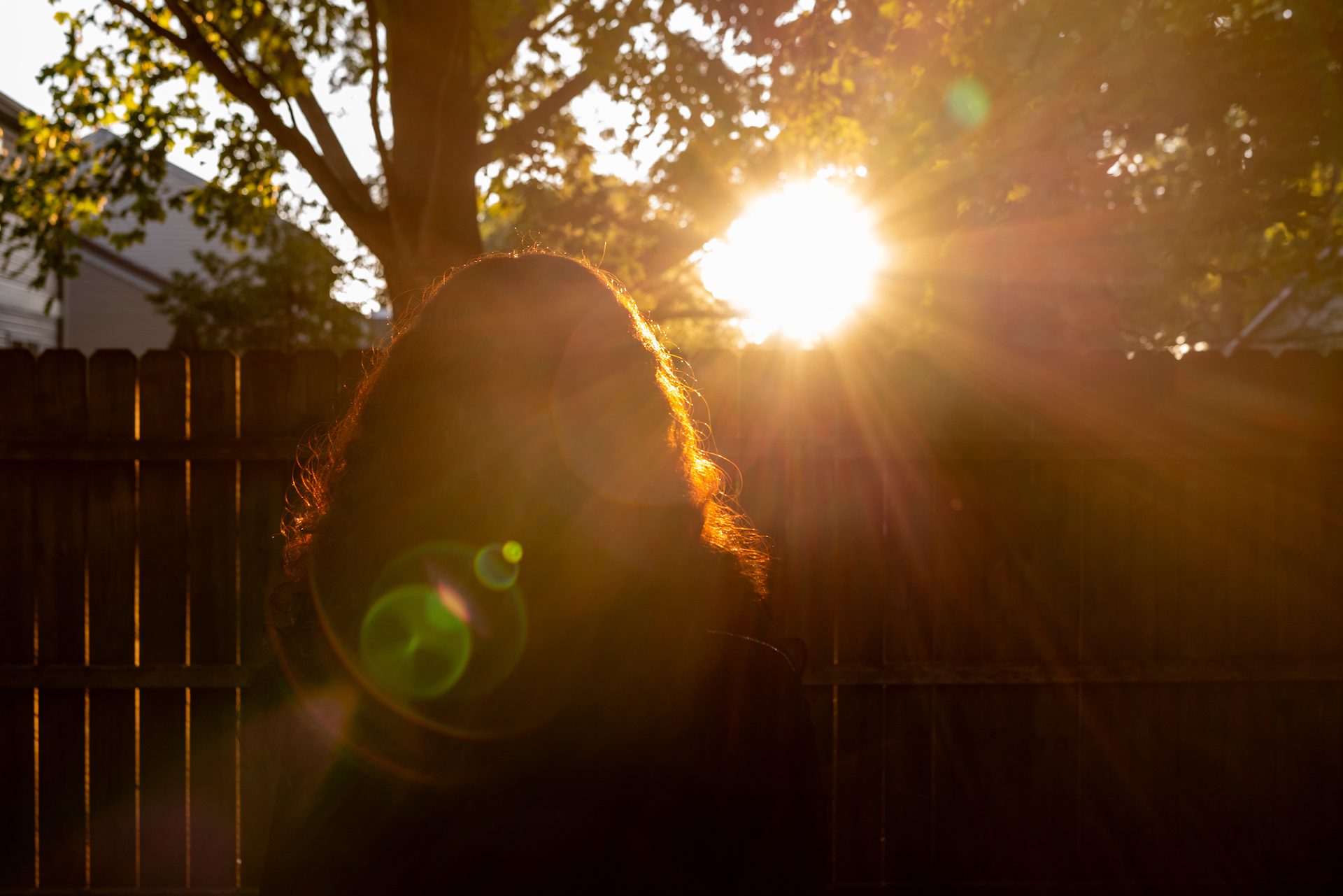 Ada views the sunset in her suburban backyard as sun rays illuminate her long hair.