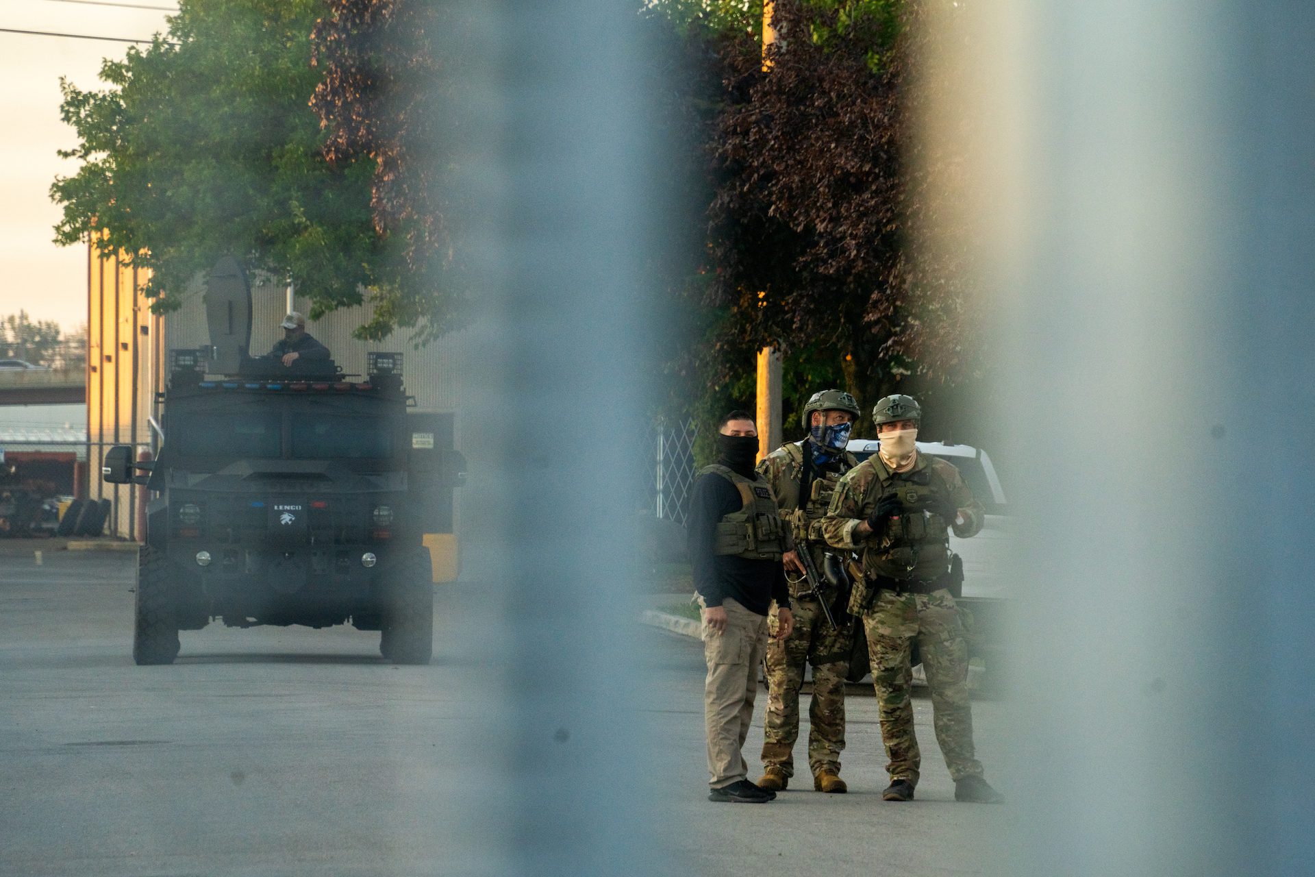 Three masked federal agents stand behind a perimeter fence at a detenion center.