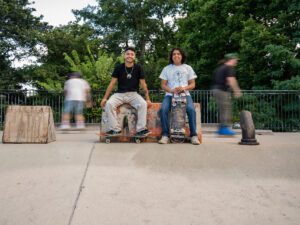 Javier Ponce (izquierda) y Rodrigo Ponce (derecha) posan para un retrato en el Wilson Skate Park de Uptown mientras los patinadores pasan detrás de ellos borrosamente.