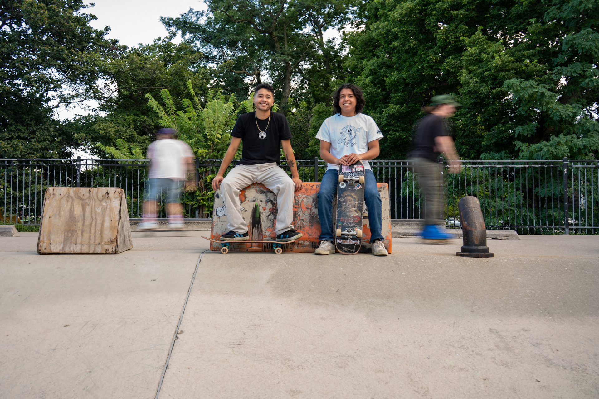 Javier Ponce (left) and Rodrigo Ponce (right) pose for a portrait at Wilson Skate Park in Uptown as skaters pass by behind them in a blur.