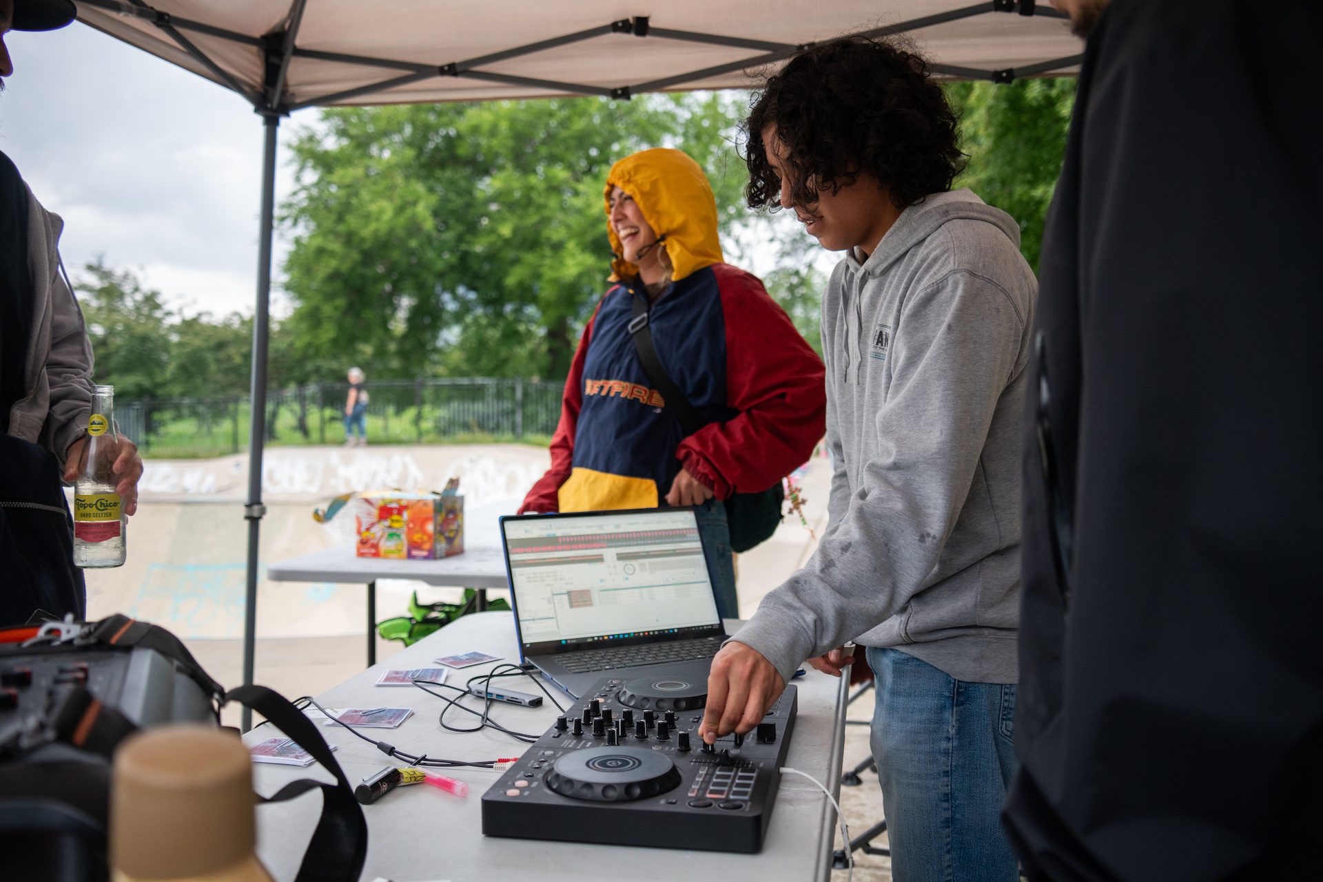 Rodrigo Ponce, 20, sets up a DJ deck and his laptop during a Boards Across Borders fundraising event in partnership with Wilson Wednesdays at Wilson Skate Park. A girl skater laughs nearby.