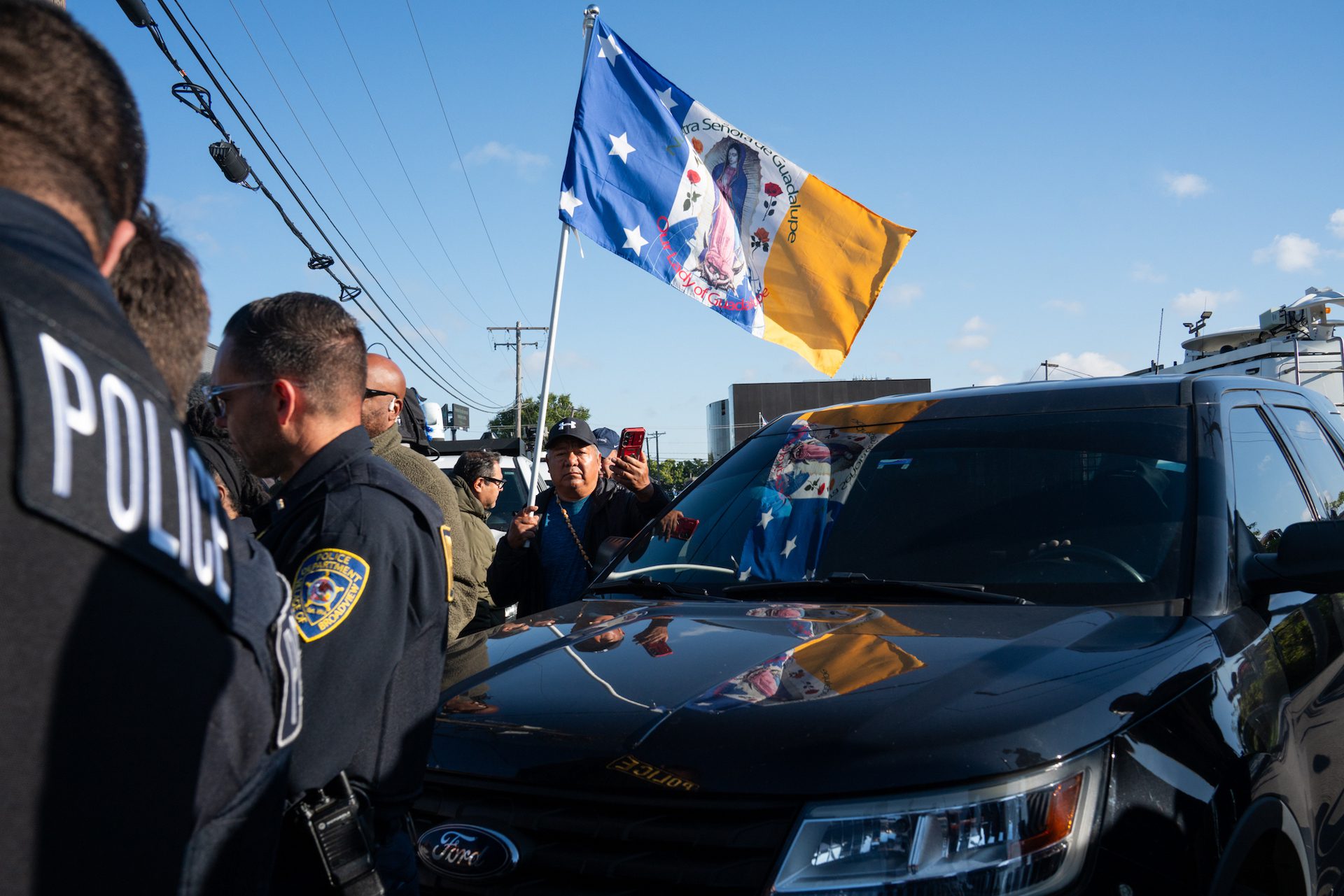 Joaquin Martinez flies a flag depicting the Virgin of Guadalupe and stands near multiple police officers as protesters block the entrance of the ICE processing facility at 1930 Beach St. during a demonstration on Friday, Sept. 5, 2025 in Broadview, Ill.