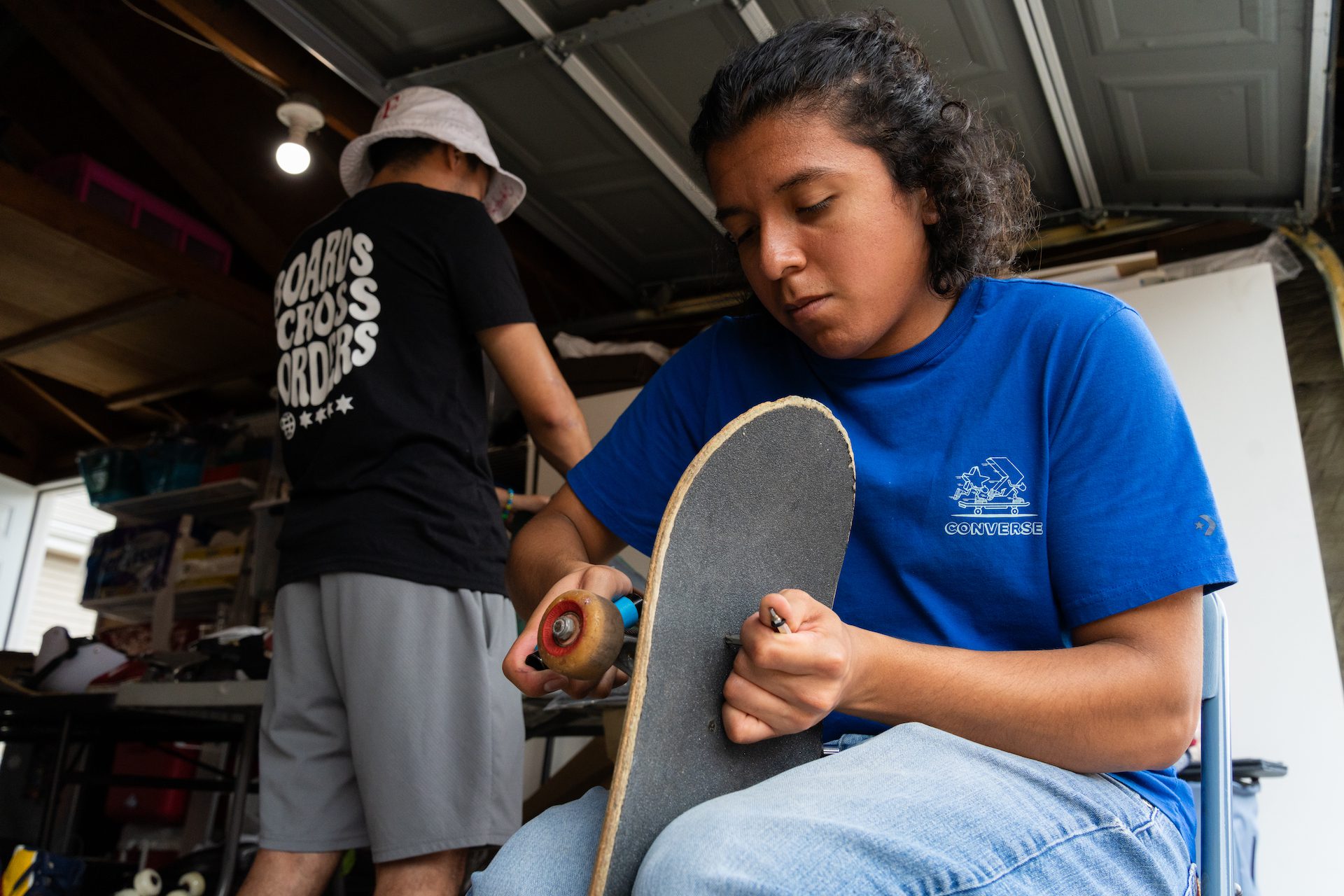 Sitting in a garage, Rodrigo Ponce detaches salvageable trucks from a waterlogged skateboard during the boxing process.