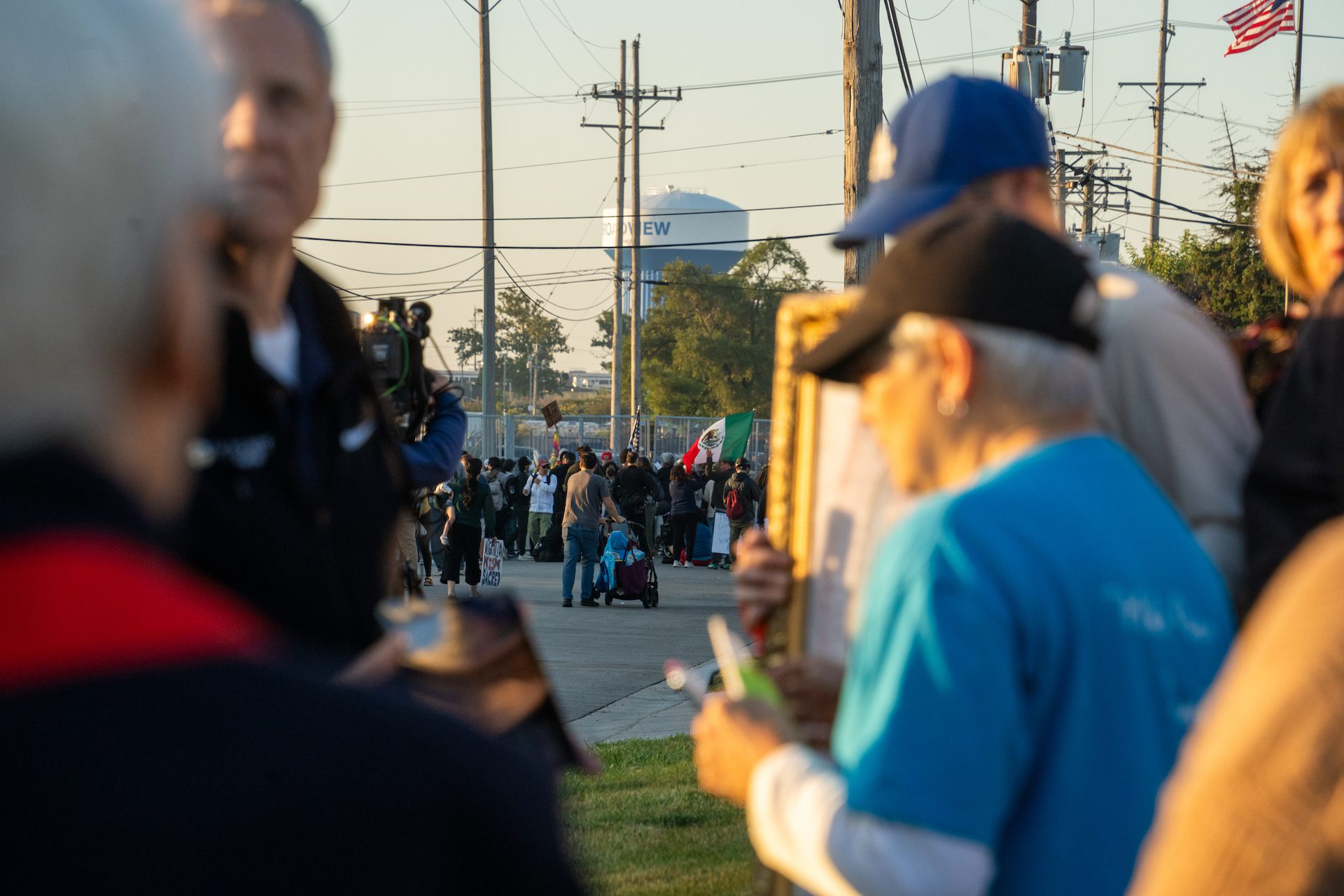 Members of the weekly prayer group begin their vigil on the corner of Beach and Lexington Street as protesters gather by the fence blocking the ICE processing center in Broadview, Ill., on Friday, Sept. 26, 2025. A larger group of protestors are seen in the distance close to the fencing around the ICE facility.