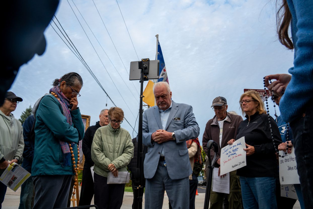 A group of several people stand in a circle praying near the Broadview ICE facility.