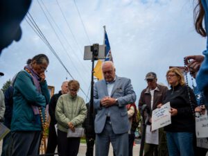 A group of several people stand in a circle praying near the Broadview ICE facility.