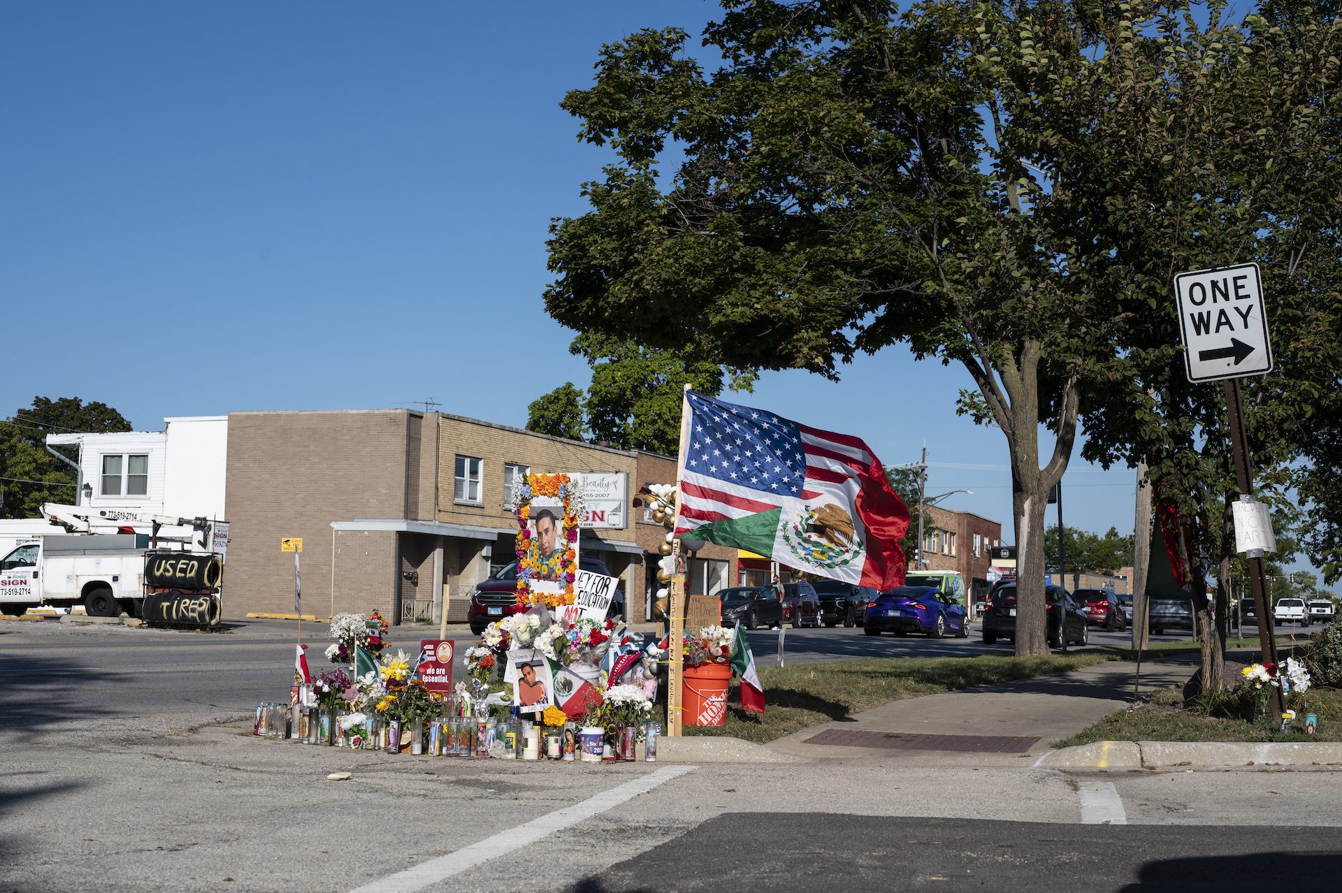 Una bandera mexicano-estadounidense ondea al viento en un monumento en memoria de Silverio Villeges-González que contiene varias velas y flores a lo largo de Grand Avenue en Franklin Park, Illinois.