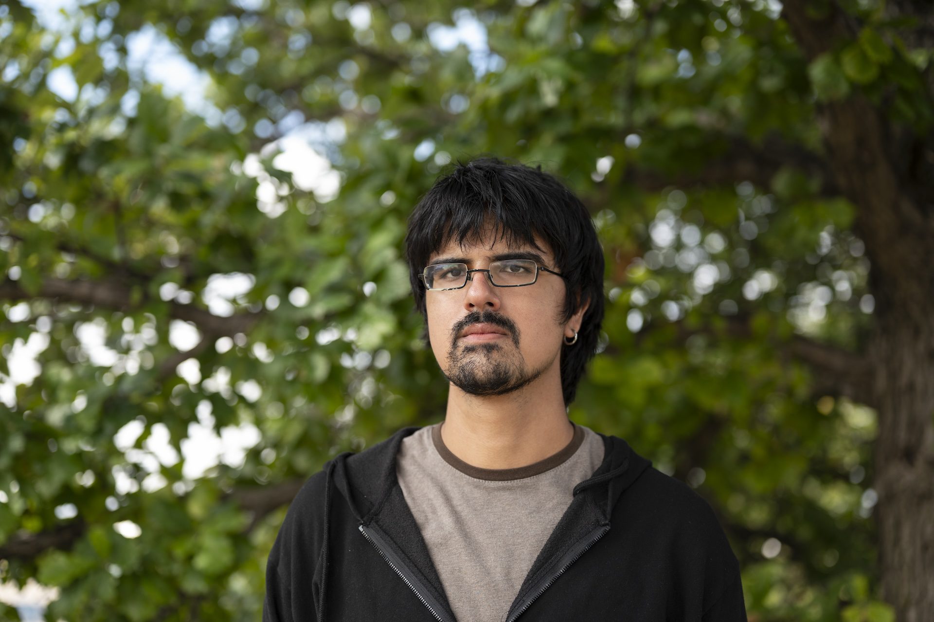 Ajay Chatha, an environmental activist, stands for a portrait in front of a tree in a riverside park.