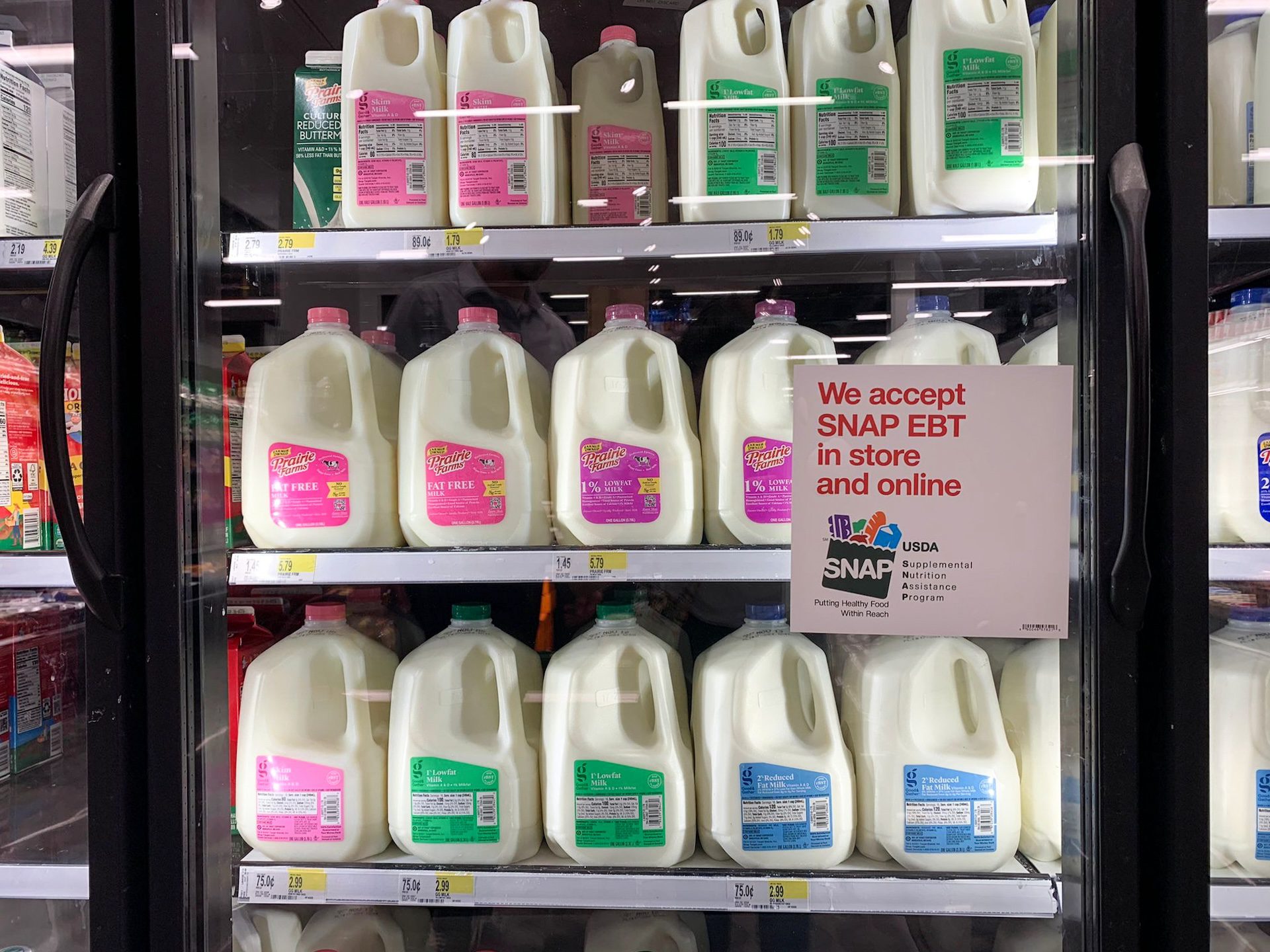 Several gallons of milk are seen in a refrigerator at a store behind a sign that says Supplemental Nutrition Assistance Program (SNAP) benefits are accepted there.