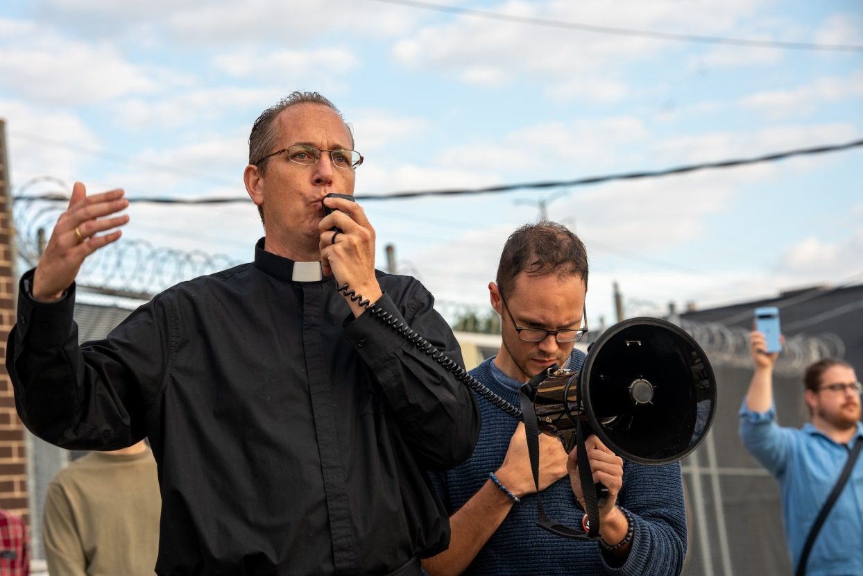 Community Organizer at The Resurrection Project and longtime faith leader Father Brendan Curran speaks into a megaphone as he rallies protesters outside the Broadview ICE facility in Broadview, IL on Sept. 12, 2025.