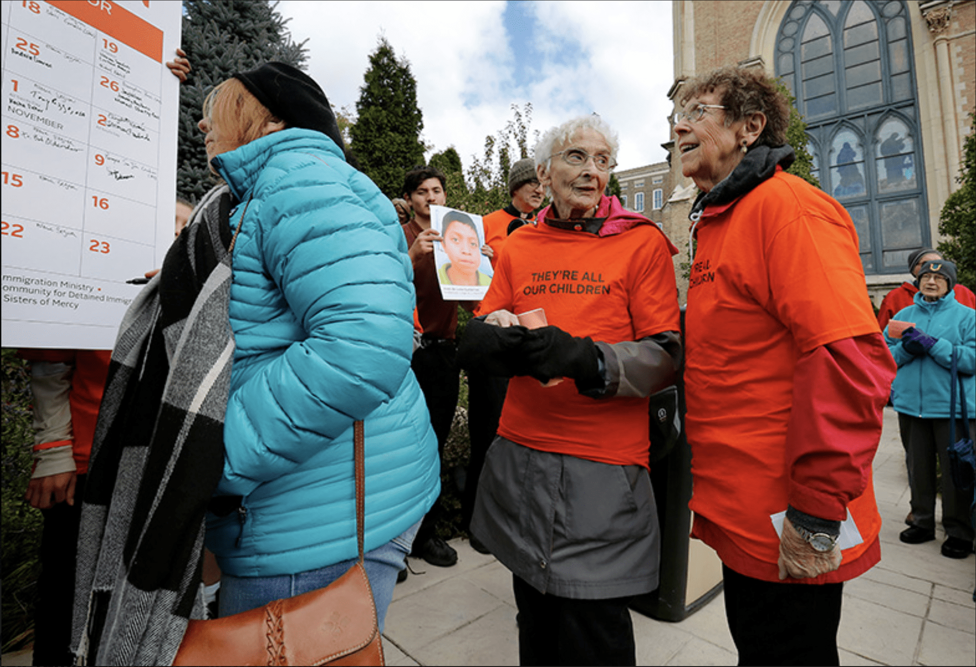 Mercy Sisters Pat Murphy and JoAnn, both wearing orange t-shirts reading, "they're all our children," stand in line as they prepare to sign a 40-day call for praying, fasting and action for immigrant children and their families.
