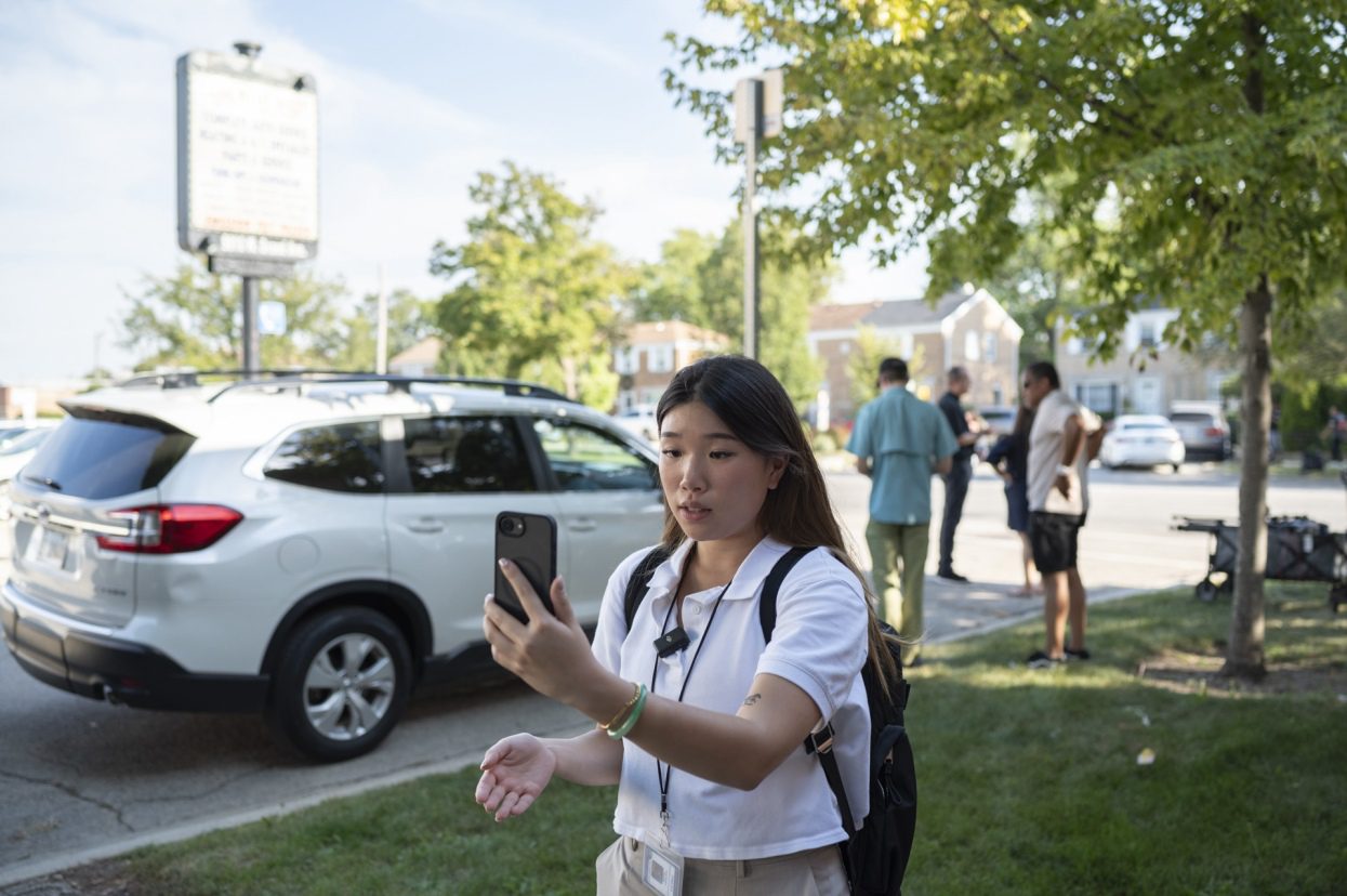 Engagement reporter Katrina Pham holds her phone out as she records a video at the corner street scene where an ICE agent fatally shot Silverio Villegas-Gonzalez in Franklin Park, IL, on Friday, Sept. 12, 2025.