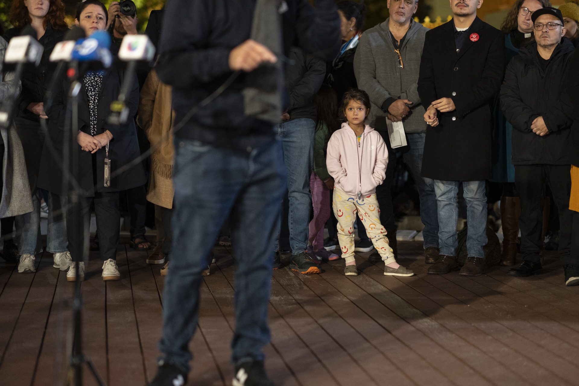 A young child, surrounded by adults, watches on as Ald. Andre Vasquez (40th) speaks to a crowd of several hundred community members at a rally at North Center Town Square on Wednesday, Nov. 5, 2025.
