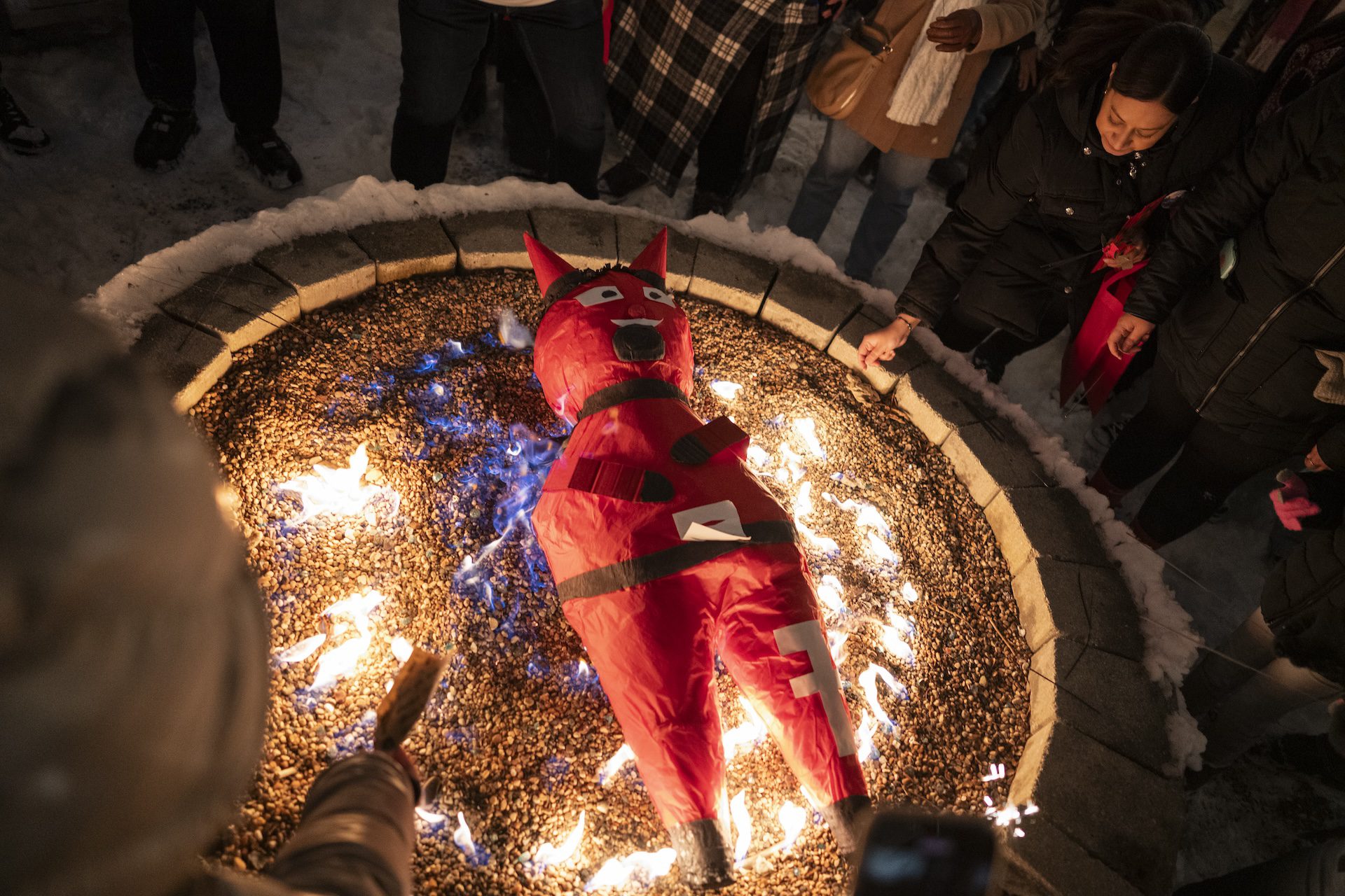 A large devil piñata burns in a circular fire pit as people drop notes to release negative experiences of 2025 into the fire at Park & Field, a bar in the Logan Square neighborhood in Chicago.