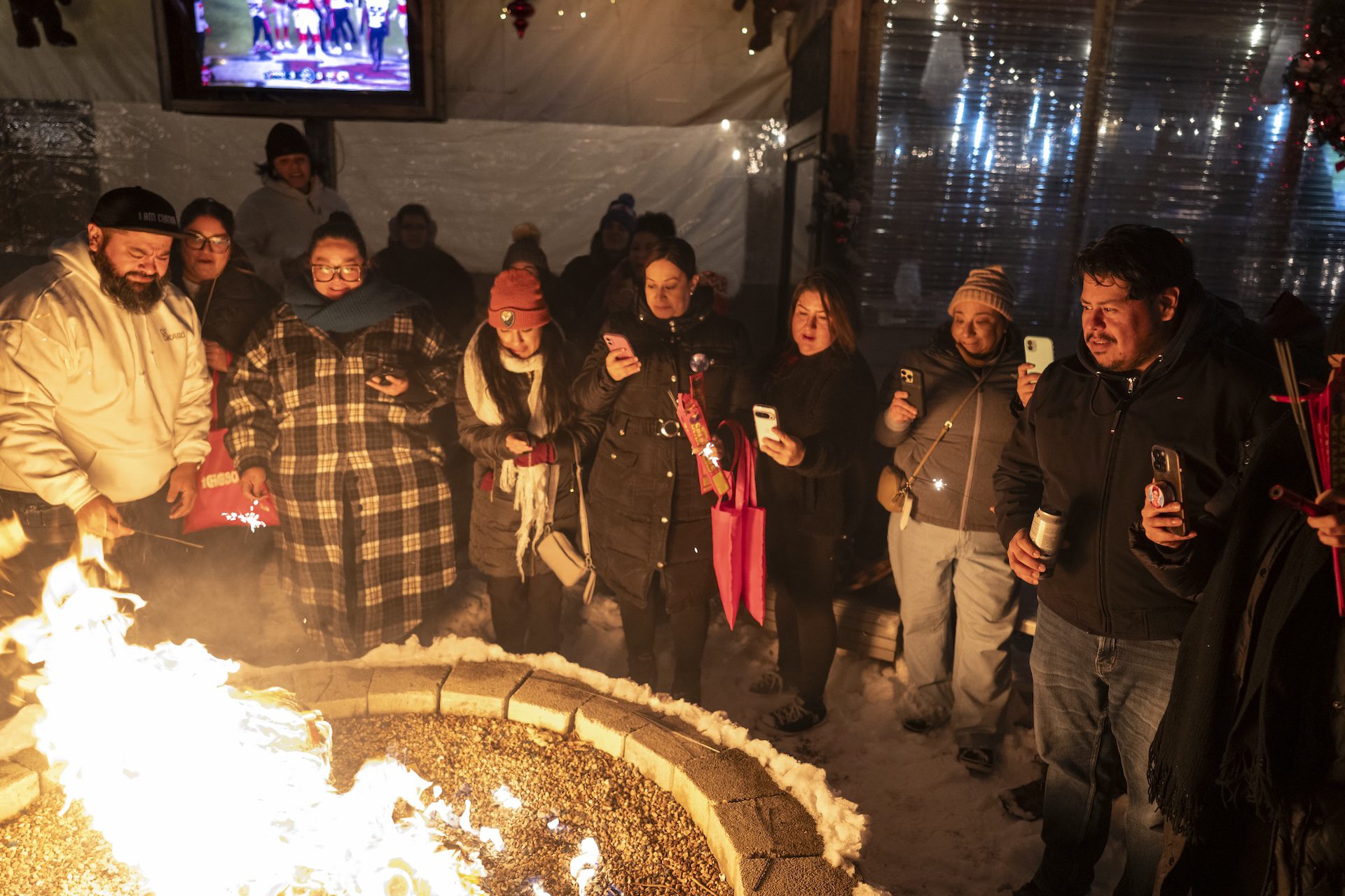 A large group of participants film on their phones as the devil piñata goes up in flames during a Quema del Diablo event at Park & Field bar in the Logan Square neighborhood of Chicago.