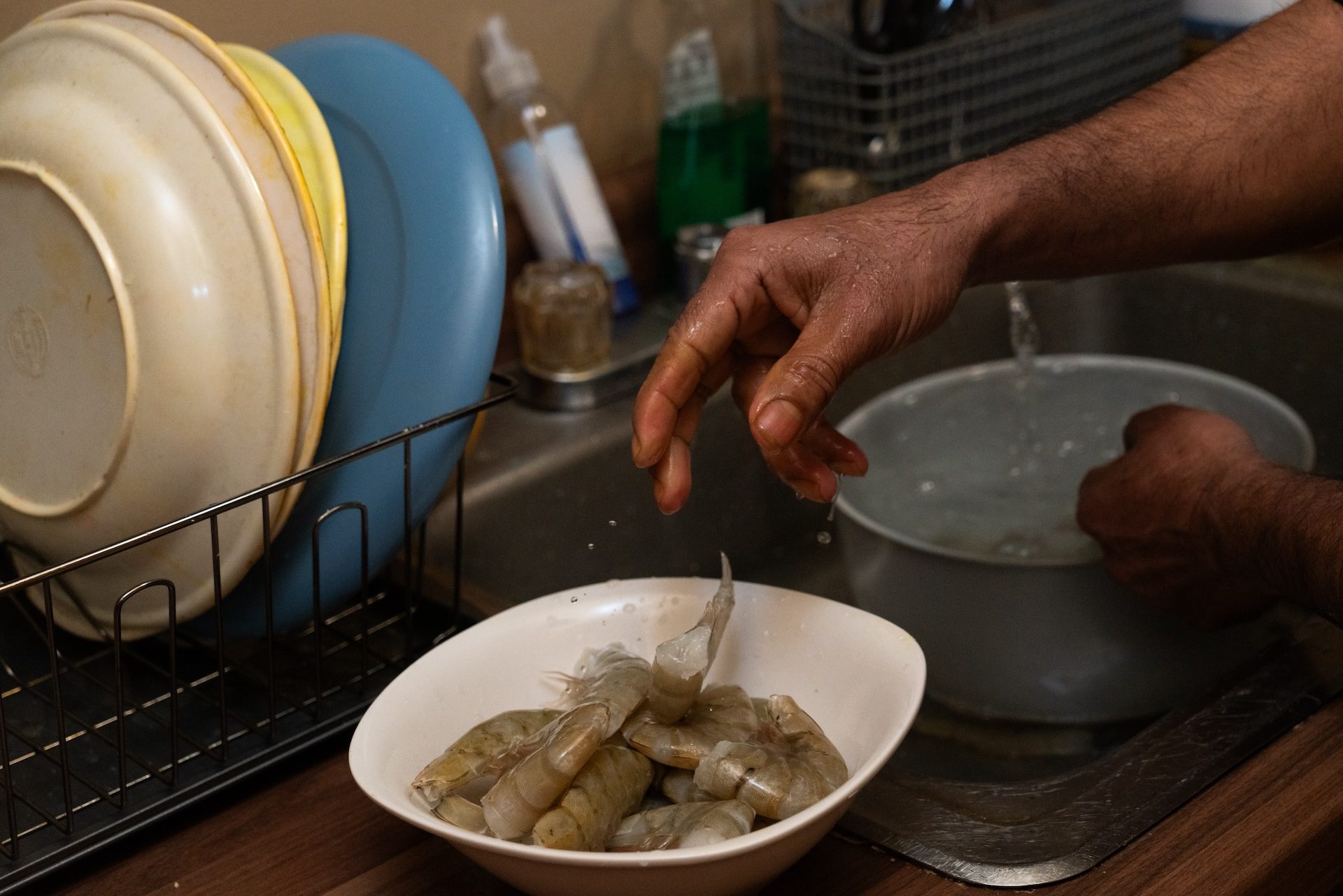 Mohamad, a Rohingya refugee, drops cleaned shrimp into a bowl as he cooks dinner in his kitchen on Jan. 14, 2026.