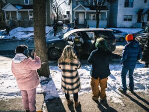 Un grupo de cinco miembros de la comunidad con abrigos observan desde la acera a los agentes del ICE mientras detienen a un hombre como parte de la Operación Metro Surge en Minneapolis, Minnesota, el 27 de enero de 2026.