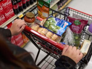 A shopper pushes a cart of groceries through a supermarket.