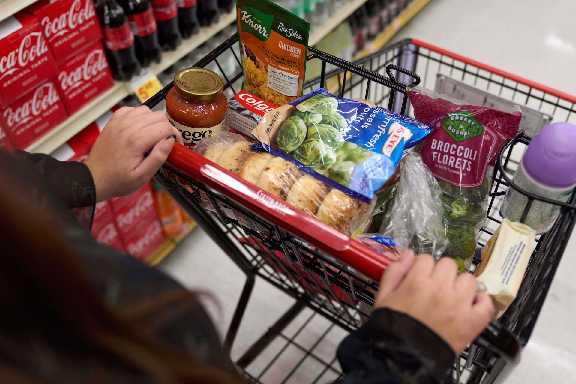 A shopper pushes a cart of groceries through a supermarket.
