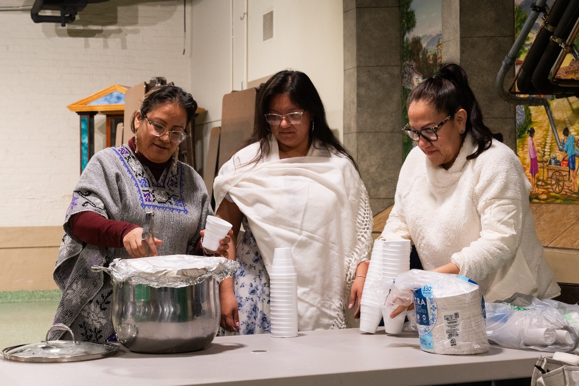 Beatriz Castillo (left) serves up champurrado, a chocolate-based beverage, in a cup for her daughter, Zitlalic Castillo (center), to enjoy between scenes during rehearsal for Pilsen’s Via Crucis procession.