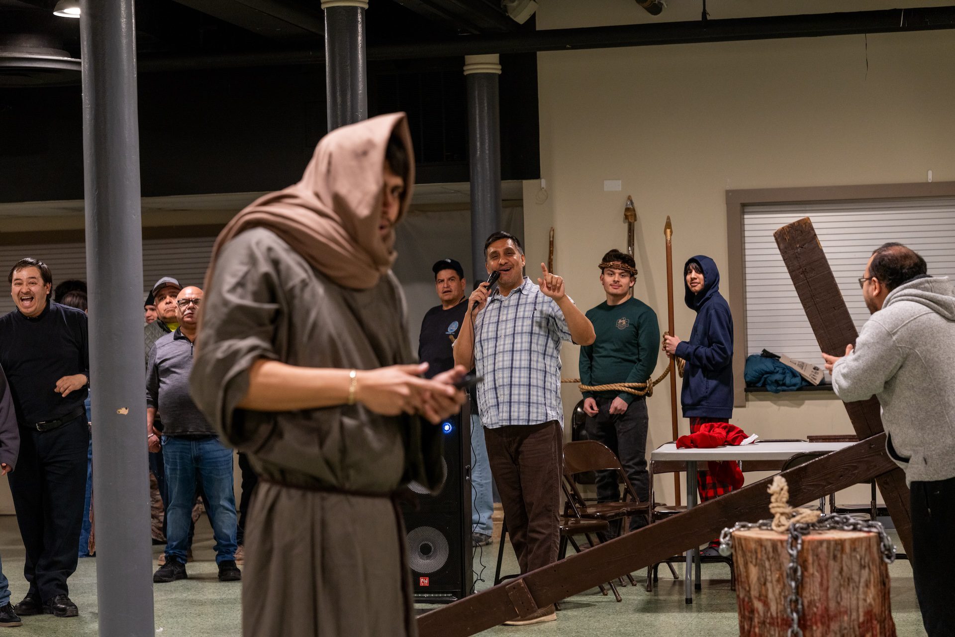 Isaac Barrera holds a microphone as he directs a large group of actors, some in costume, during a rehearsal for Pilsen’s Via Crucis procession.