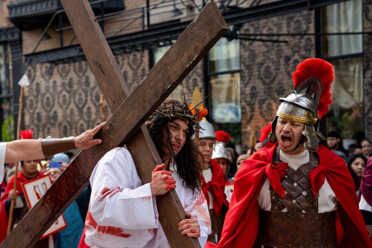 An actor playing Jesus carries a large cross as an actor playing a solider yells at him during the Via Crucis procession along 18th Street in Pilsen.