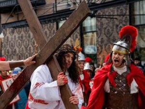 An actor playing Jesus carries a large cross as an actor playing a solider yells at him during the Via Crucis procession along 18th Street in Pilsen.