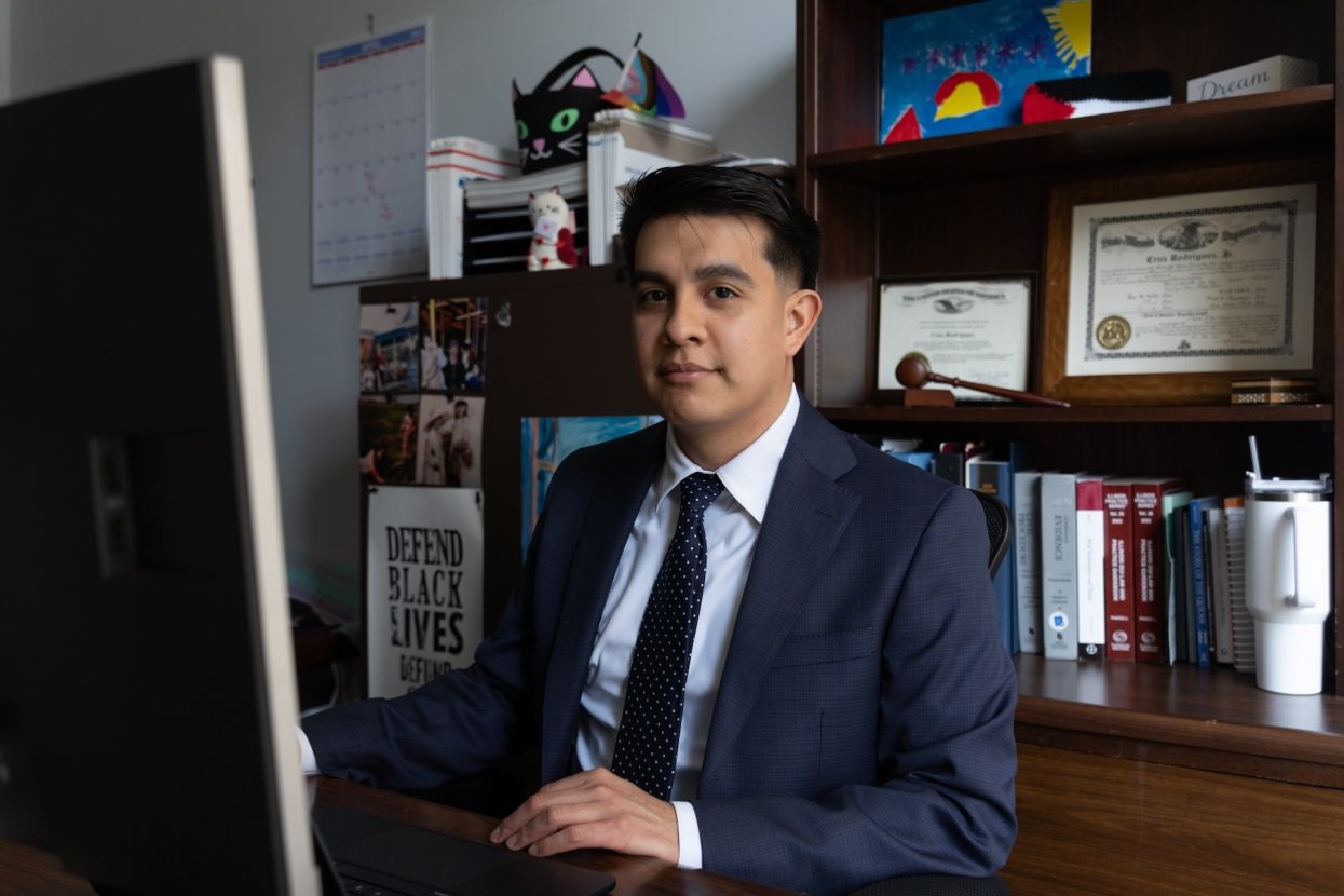 Cook County public defender Cruz Rodriguez sits at his desk in front of his computer. A gavel and degrees sit on the shelves behind him.