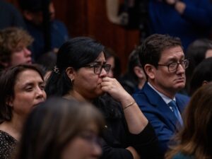 A group of audience members watch carefully as video footage shows footage of ICE officers interacting with protesters during a hearing.