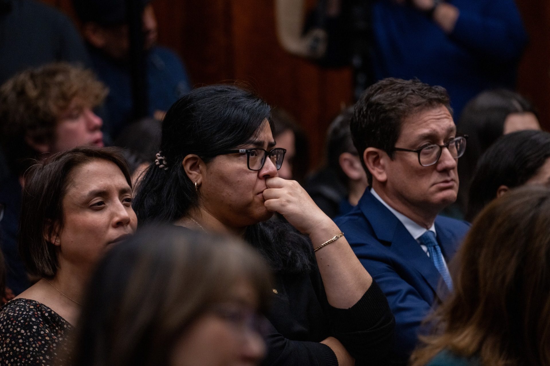 A group of audience members watch carefully as video footage shows footage of ICE officers interacting with protesters during a hearing.