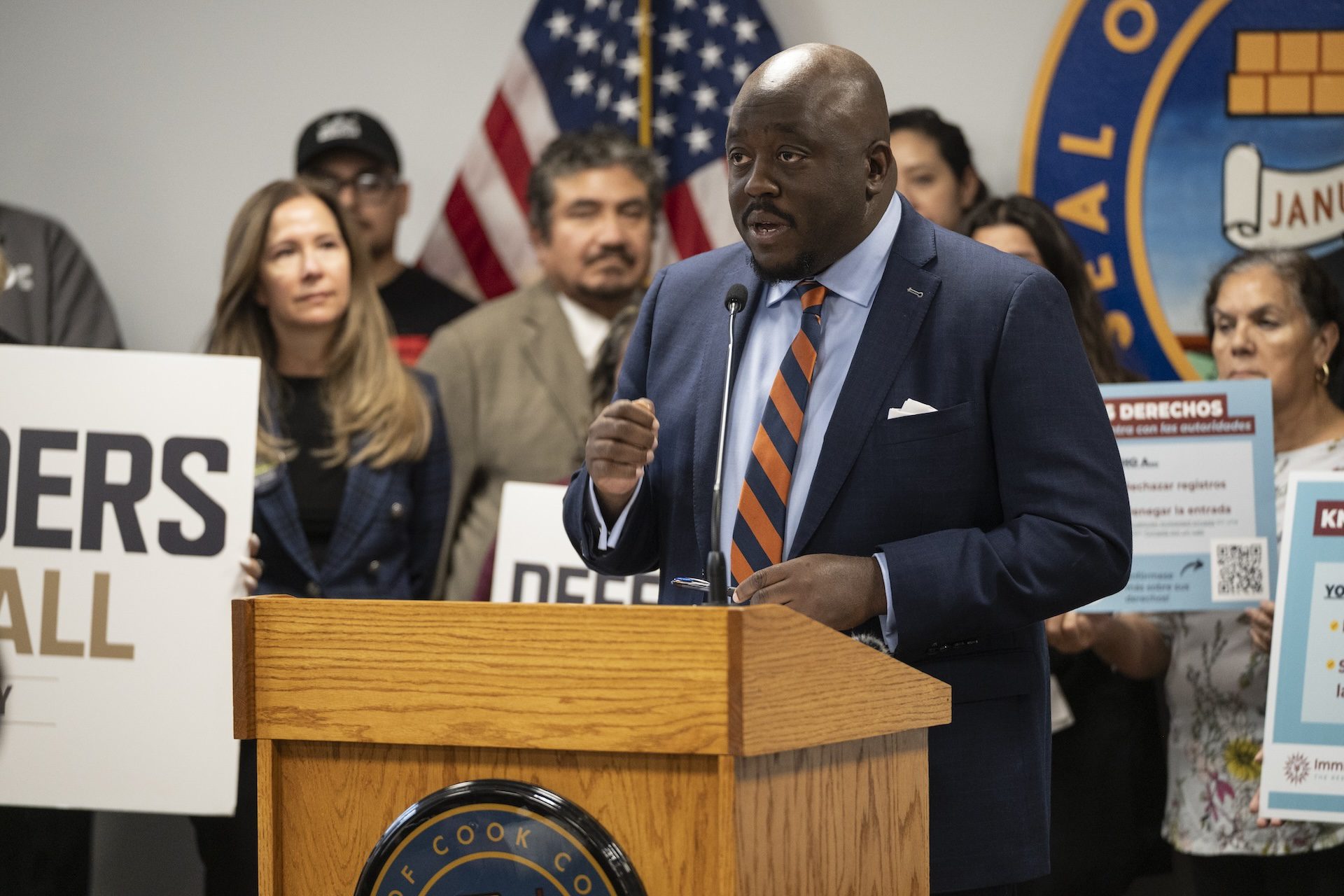 Cook County Public Defender Sharone Mitchell speaks stands at podium speaking among group of supporters of expanding the public defender immigration unit.