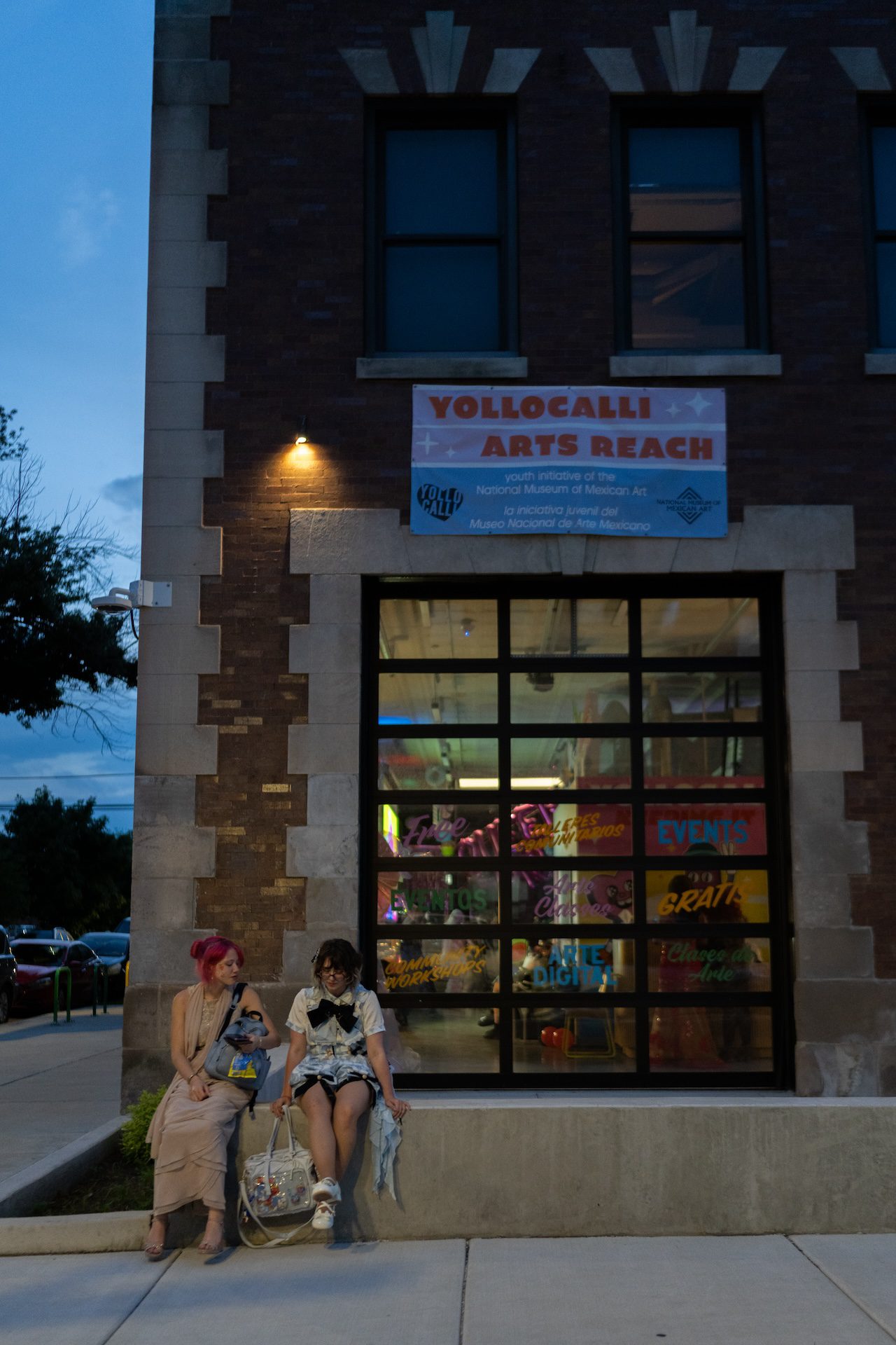 Queer prom attendees sit on a concrete ledge as they wait for rides outside of the Yollocalli Arts House fire station at the end of the night on June 13, 2025.