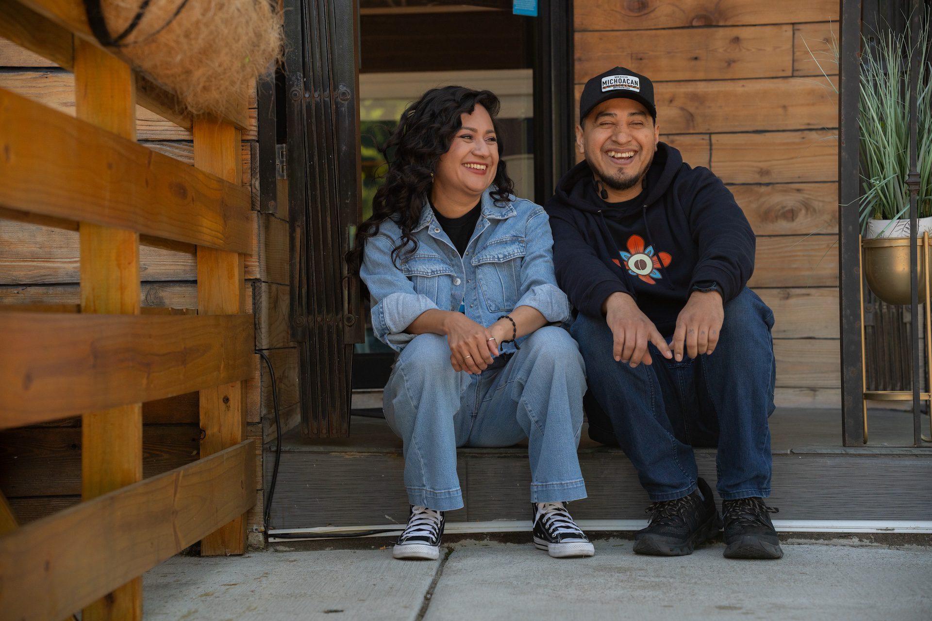 Rocio Villalva (izquierda) y Omar Contreras (derecha) ríen juntos mientras posan para un retrato afuera de la puerta principal de Dulce De Leche Cafecito en North Center el lunes 11 de mayo de 2026.