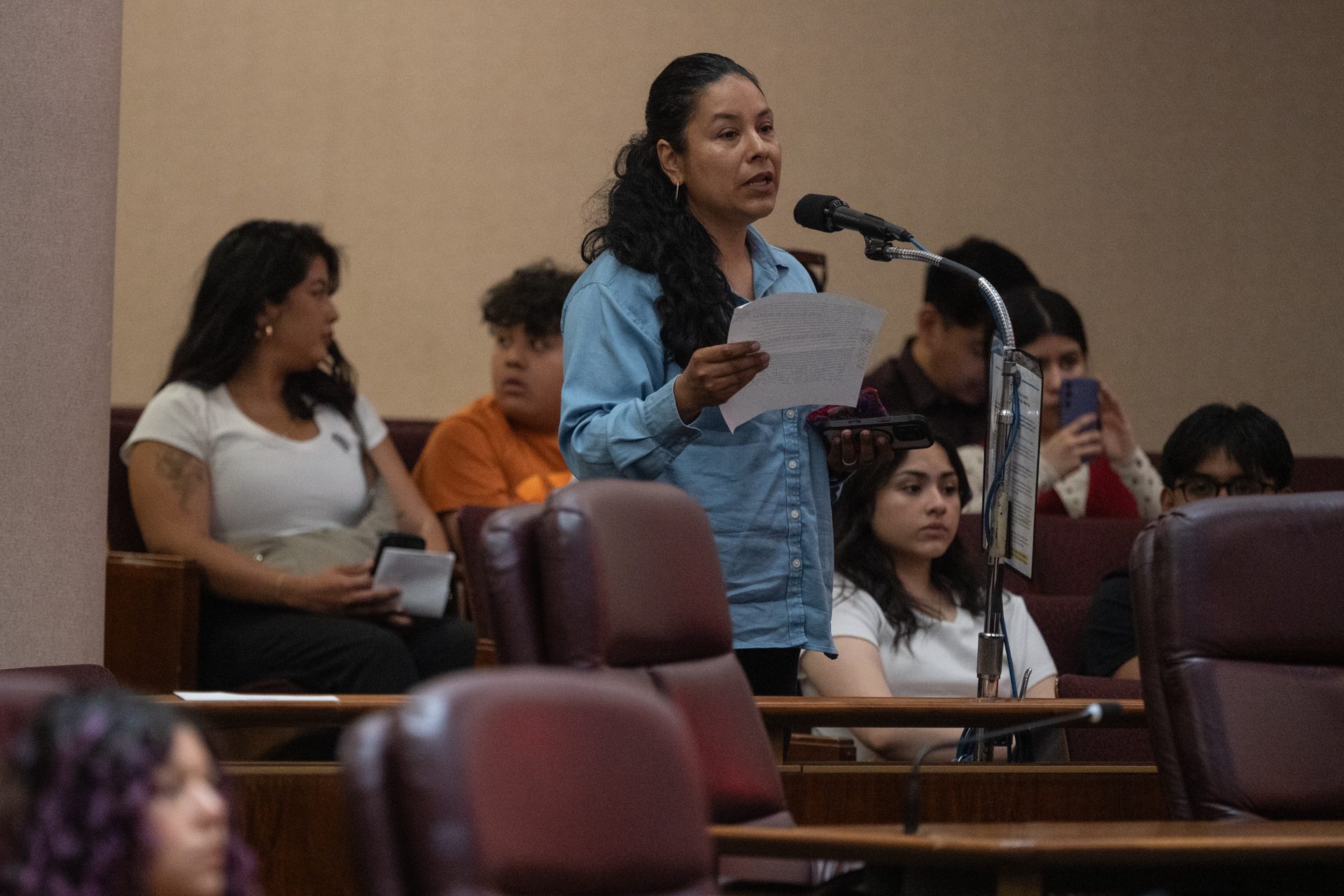 Claudia Marchan, the executive director of Northern Illinois Justice for Our Neighbors and a former DACA recipient, stands at a microphone speaking in support of preserving and expanding the DACA program during a Committee on Immigrant and Refugee Rights hearing on June 11, 2026.