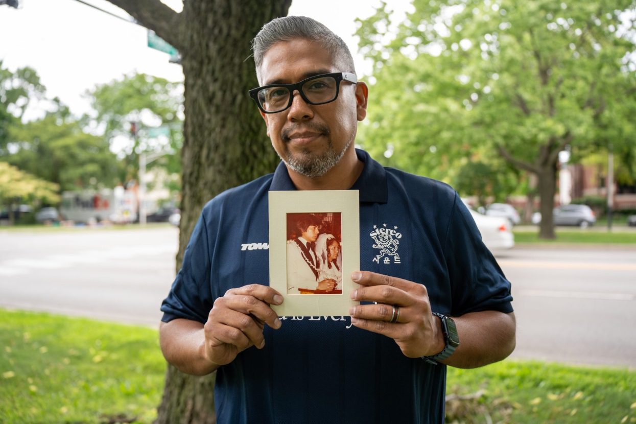 David Hernandez stands outside near a tree as he holds a photograph of his parents' wedding, taken around 1968, in Logan Square.