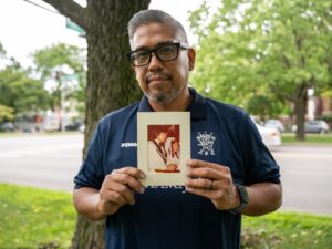 David Hernandez stands outside near a tree as he holds a photograph of his parents' wedding, taken around 1968, in Logan Square.