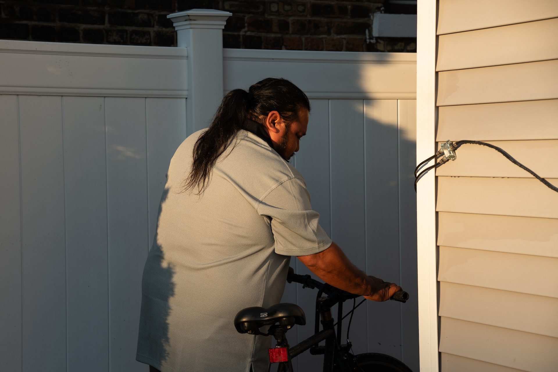 Gualberto Olac abre y saca su bicicleta de su patio mientras se dirige al trabajo una mañana de junio.