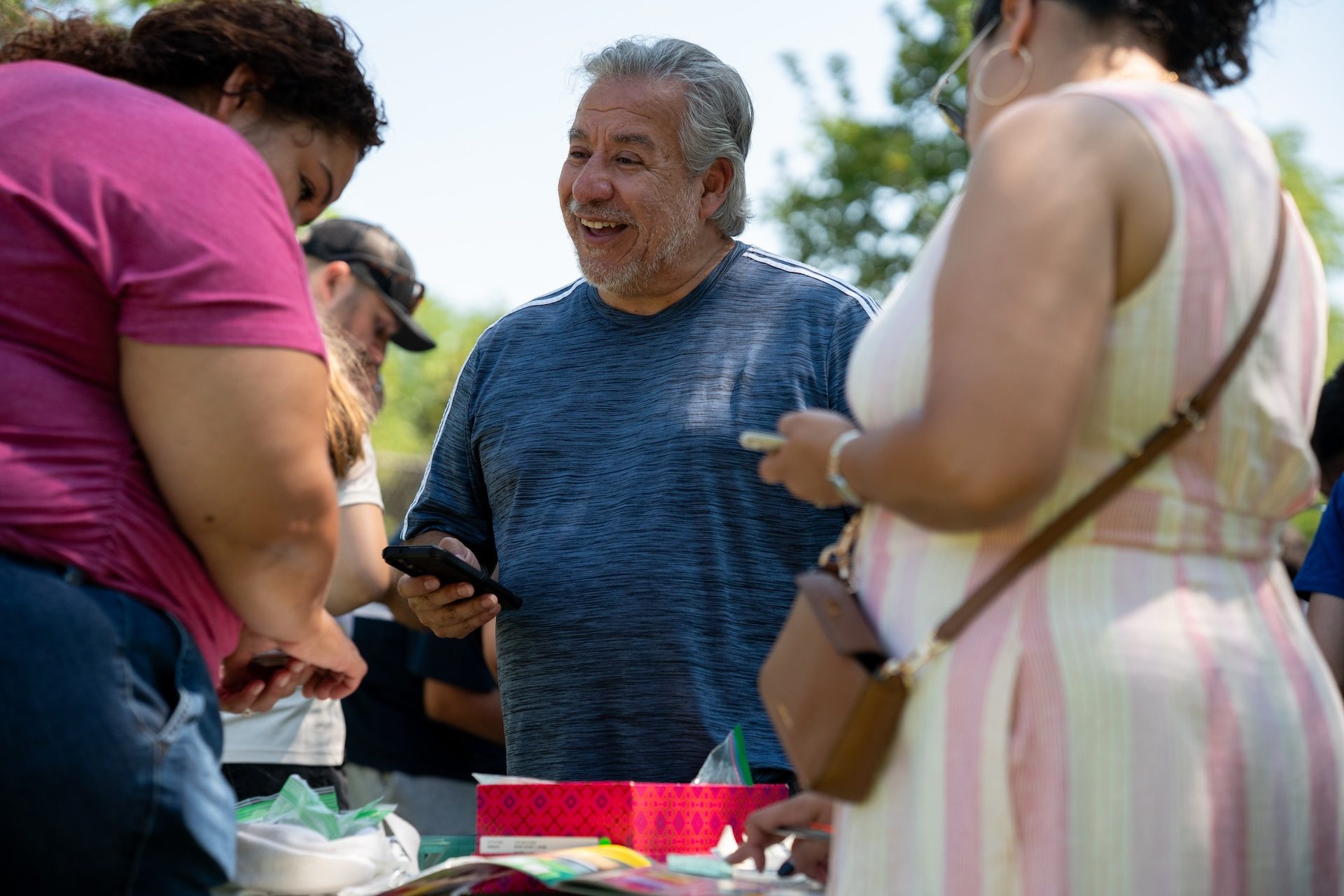 Guillermo Vidaurre smiles as he negotiates trades with fellow collectors at a table during an outdoor Panini swap event in Portage Park on July 12, 2026.