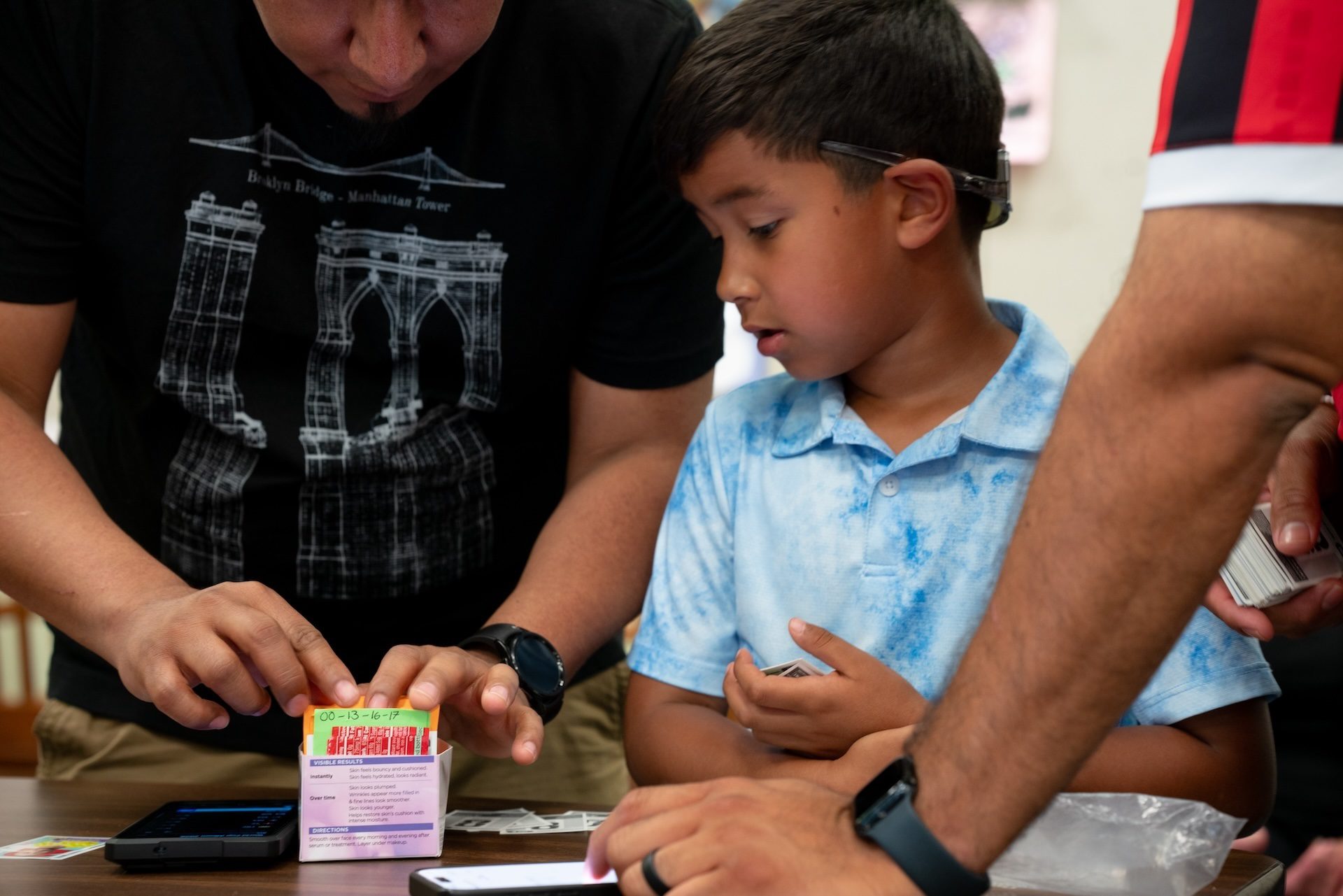 A young Panini sticker collector looks on as an adult collector sorts through their collections looking for trades during the Logan Square Library Branch Panini swap event on June 28, 2026.