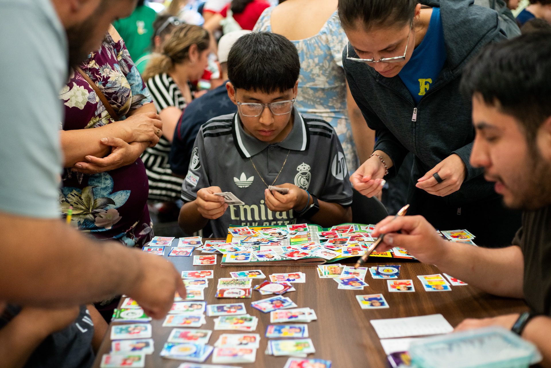 Anthony Cahuatijo, 13, is surrounded by adults at a table as he sorts his new stickers by country before adding them to his Panini album during the Logan Square Library Branch Panini swap event on Sunday, June 28, 2026.